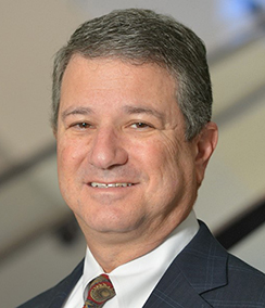Larry Kunin headshot, Middle aged Caucasian man with grey hair smiling. He is wearing a blue suit with a red tie.