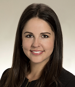 Laura Ross headshot Caucasian Woman in a black dress, smiling with pink lipstick, long dark brown hair, brown eyes