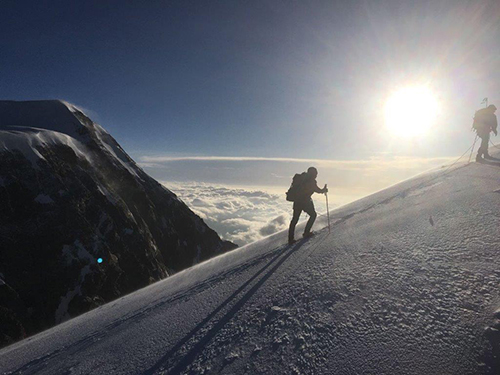 Wes Climbing_Edited Image of Two Men climbing a tall snowy mountain with clouds and sun in the background