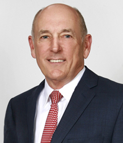 Wes Reede headshot, Older Caucasian man in a navy blue suit with white shirt and red tie, grey hair, smiling