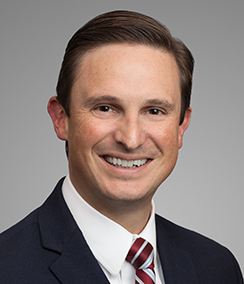 Jeff Wilcox headshot, a Caucasian man with brown hair and brown eyes in a black suit with a white shirt and red striped tie. He is smiling.