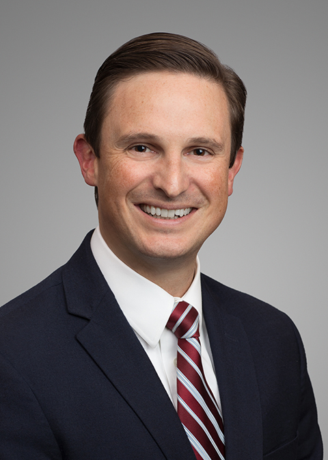 Jeff Wilcox headshot, a Caucasian man with brown hair and brown eyes in a black suit with a white shirt and red striped tie. He is smiling.