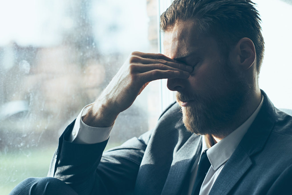 Caucasian Man in a suit suffers from fatigue and perhaps insomnia, He is tired and stressed out. He takes a break and covers his eyes.
