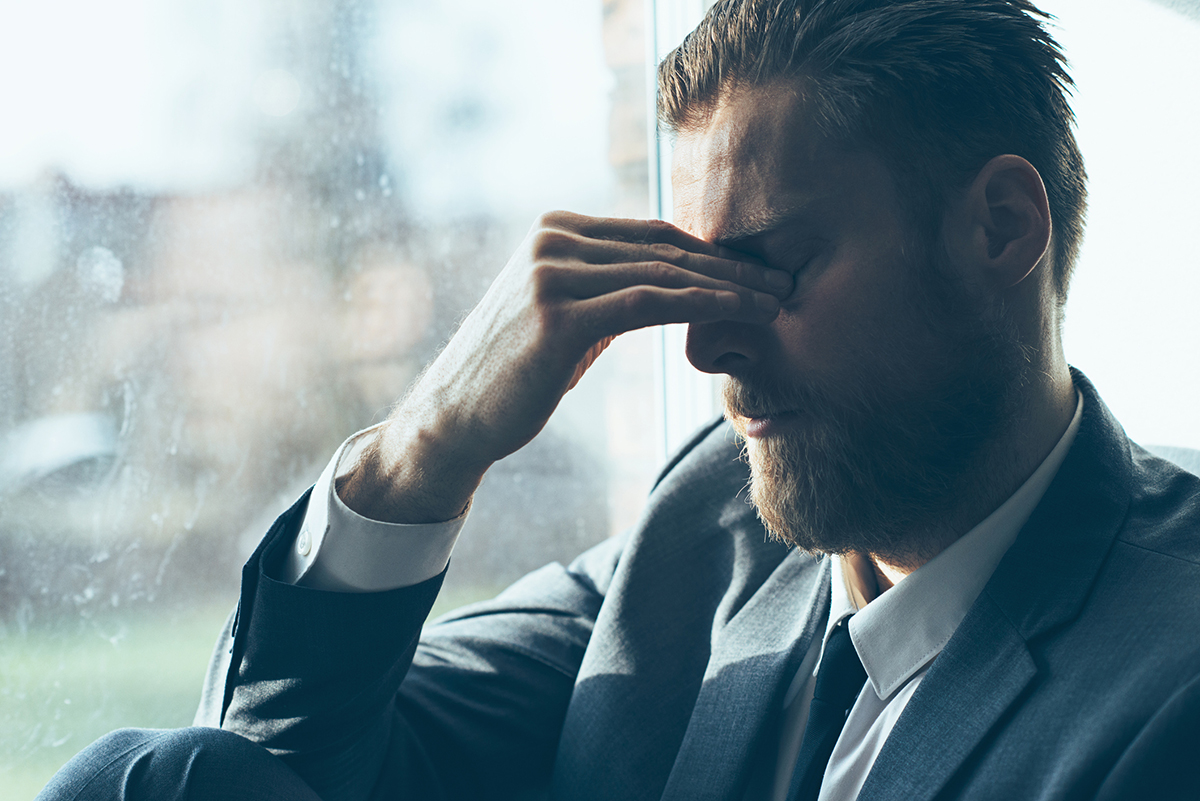 Caucasian Man in a suit suffers from fatigue and perhaps insomnia, He is tired and stressed out. He takes a break and covers his eyes.