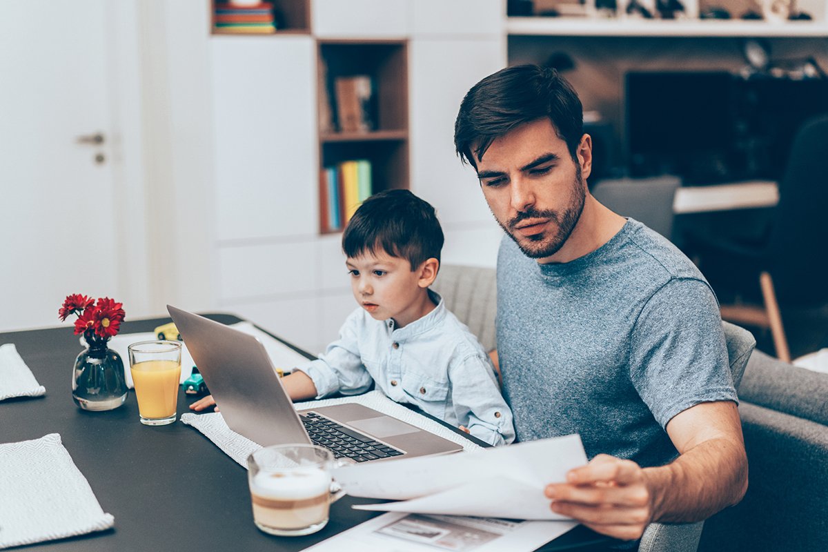 Handsome father working with documents and laptop at home with his little son
