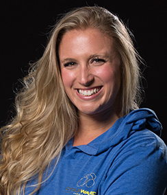 Emily Romano headshot, a young Caucasian woman with long blonde hair wearing a blue activewear shirt with a hood