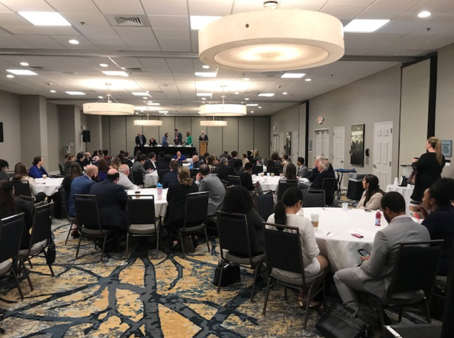 Government Lawyers Committee, Business Professionals in a large meeting room, man at a podium, people behind a table on stage Government Lawyers Committee, Business Professionals in a large meeting room, man at a podium, people behind a table on stage