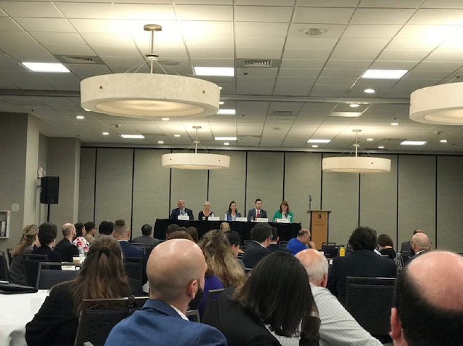 Government Lawyers Committee Update 8 Government Lawyers Committee, Business Professionals in a large meeting room, people behind a table on stage, symposium
