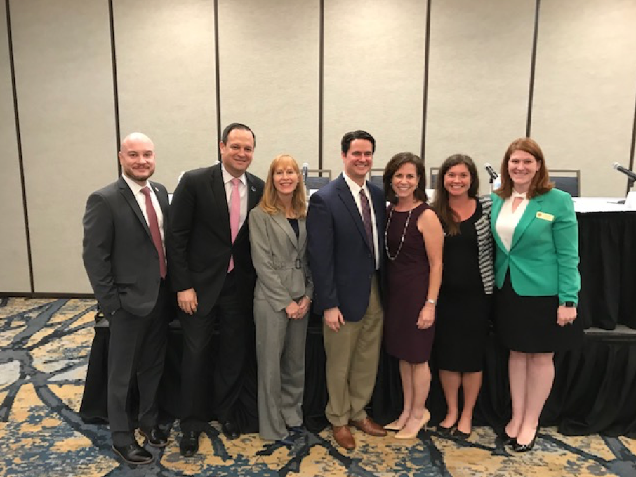 Government Lawyers Committee Update seven people standing and smiling, four caucasian women, three caucasian men, professional dress, business suits, dress, blazer, skirt