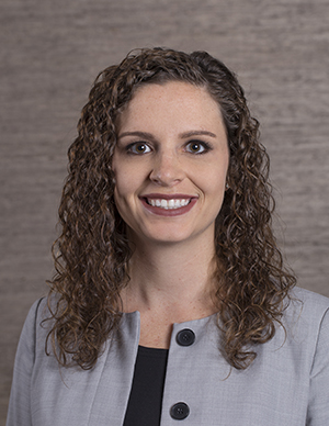 Young caucasian woman, curly brown hair, brown eyes, grey jacket with black top